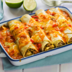 Four shredded beef enchiladas in a white 9x13-inch baking dish with a cut lime in the background.