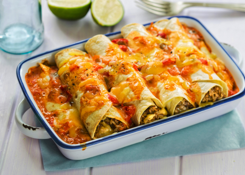 Four shredded beef enchiladas in a white 9x13-inch baking dish with a cut lime in the background.