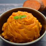 Mashed sweet potato dip in a bowl with a green garnish and a sliced sweet potato in the background.