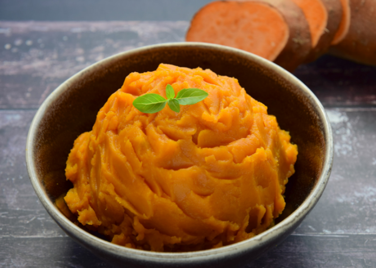 Mashed sweet potato dip in a bowl with a green garnish and a sliced sweet potato in the background.