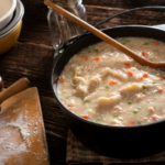 A large pot of chicken and dumplings with a wooden spoon.