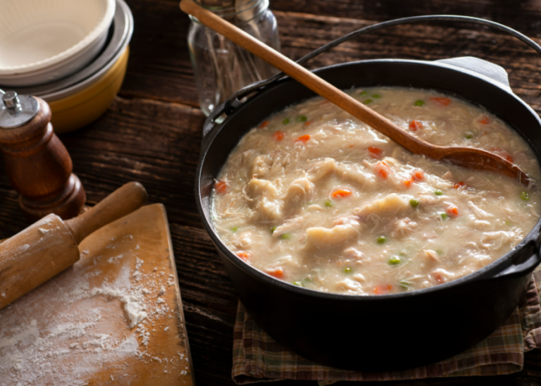 A large pot of chicken and dumplings with a wooden spoon.