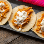 Three chicken tinga tacos on a black plate topped with queso fresco.