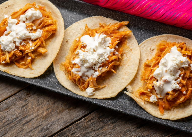 Three chicken tinga tacos on a black plate topped with queso fresco.