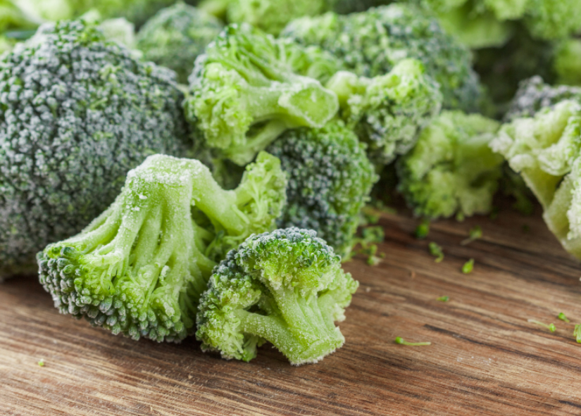 A bunch of frozen broccoli florets on a wooden surface.