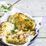 Three pieces of grilled cabbage on a platter with a dipping sauce in the background.