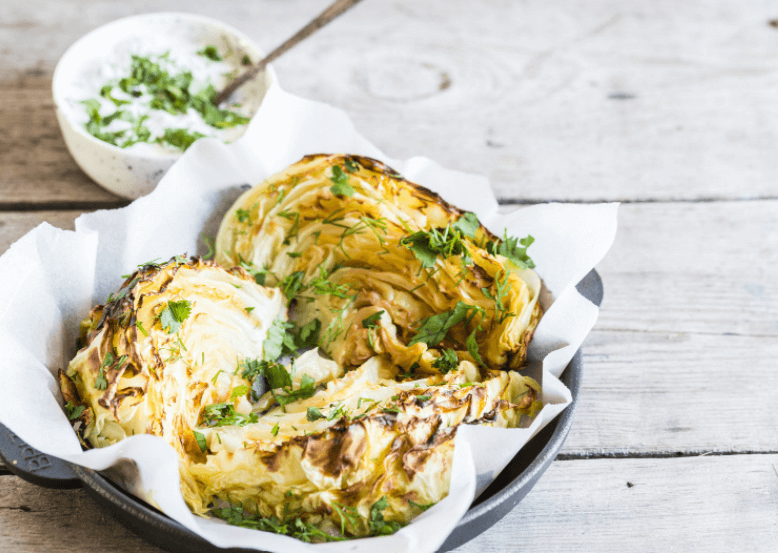 Three pieces of grilled cabbage on a platter with a dipping sauce in the background.