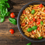 A large skillet with filled with a vibrant penne pasta, cherry tomatoes, and basil.