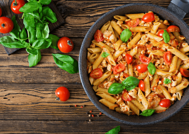 A large skillet with filled with a vibrant penne pasta, cherry tomatoes, and basil.