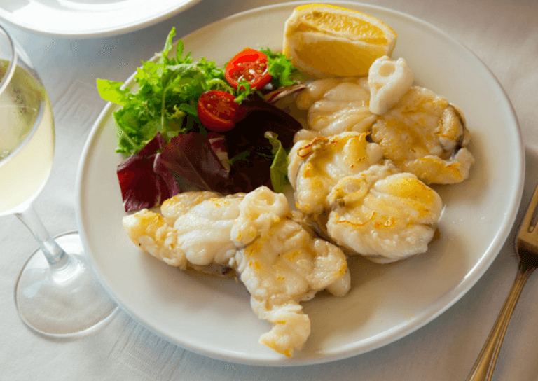 Monkfish fillets with greens and a lemon wedge on the side.