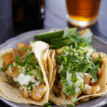 Two pollock fish tacos topped with cilantro and cheese.