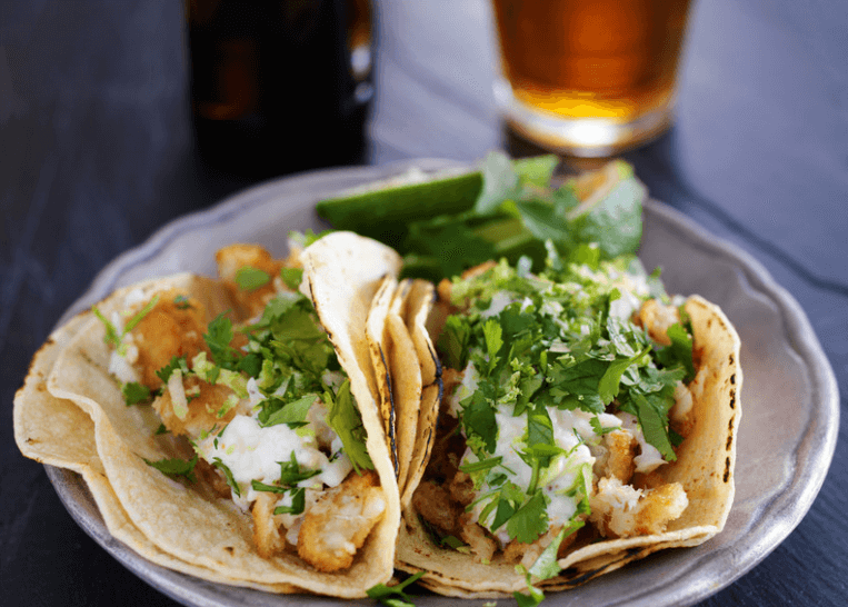 Two pollock fish tacos topped with cilantro and cheese.