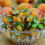 A clear glass bowl filled with apricot salsa including chopped herbs and onions.