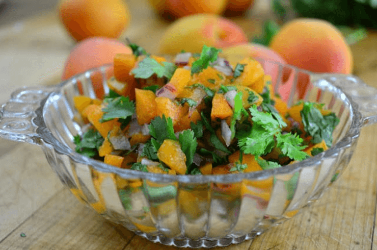 A clear glass bowl filled with apricot salsa including chopped herbs and onions.