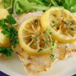 Fish fillet with two slices of lemons garnished with green herbs.