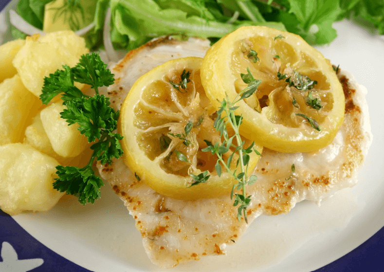 Fish fillet with two slices of lemons garnished with green herbs.