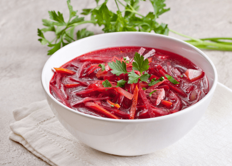 A white bowl full of borscht with some green herbs in the background.