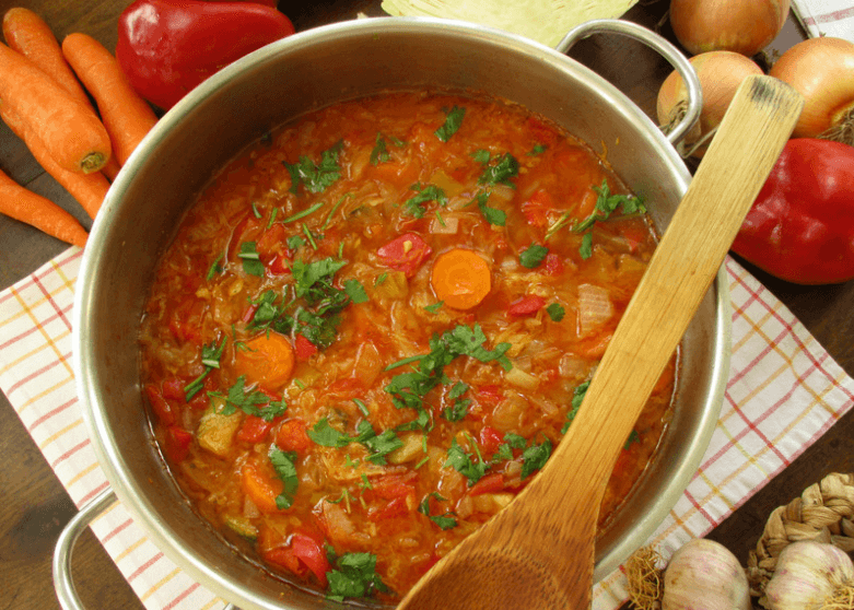 Large pot of cabbage soup with a wooden spoon on top of the pot.