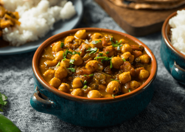 A small blue bowl filled with chana masala, with rice and other side dishes in the background.