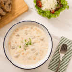 A bowl of creamy clam chowder with sliced bread and a salad on the side.
