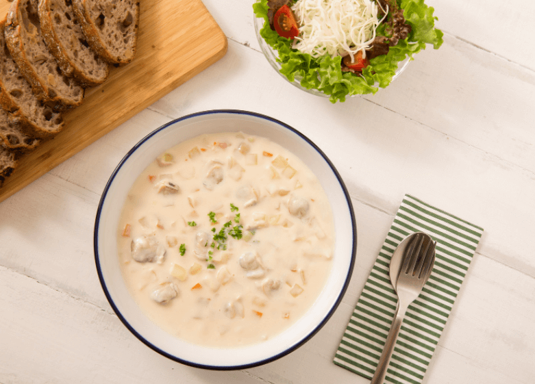 A bowl of creamy clam chowder with sliced bread and a salad on the side.