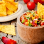 A wooden bowl of peach salsa with tortilla chips in the background.