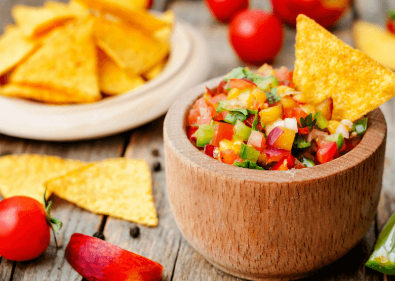 A wooden bowl of peach salsa with tortilla chips in the background.