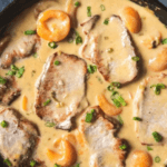 A large skillet with pork chops in a creamy apricot sauce.