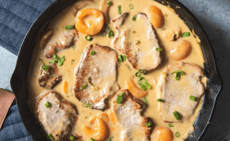 A large skillet with pork chops in a creamy apricot sauce.