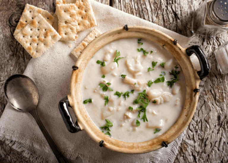A bowl of fish chowder with saltine crackers on the side.