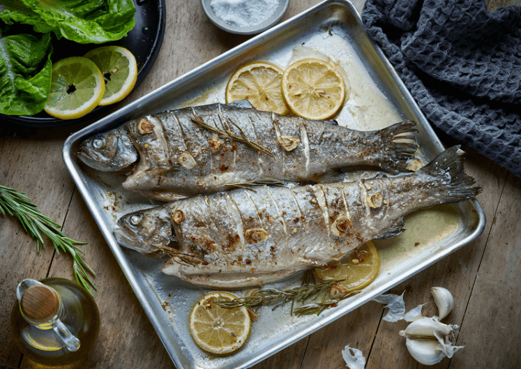 Two whole fish on a baking pan with slices of lemon.