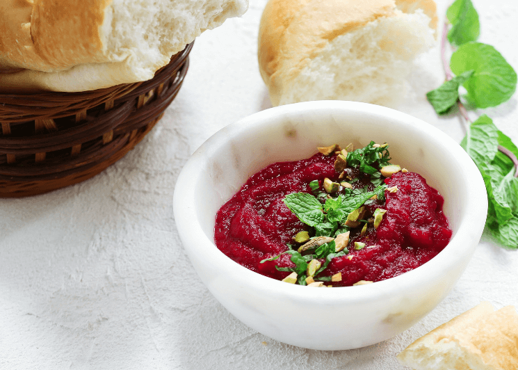Beet dip in a white bowl garnished with green herbs and with bread on the side.
