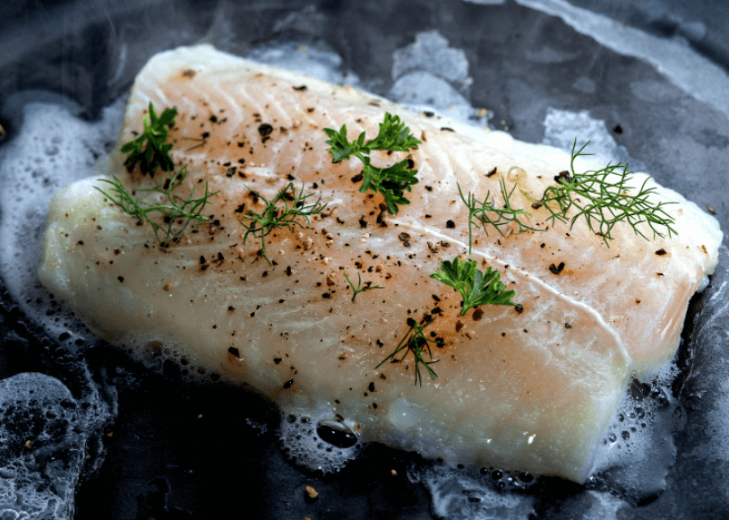 Fillet of white fish being cooked on a pan.