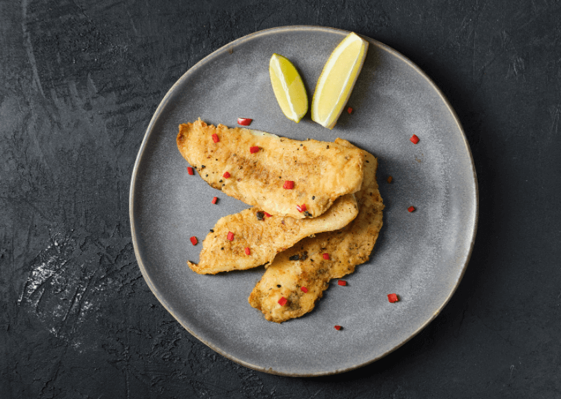 Three fillets of pan-fried white fish with two lemon wedges on the side.