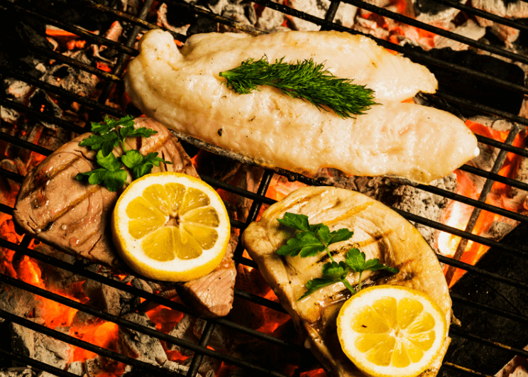 Fish fillets being grilled with herbs and lemon slices on top.