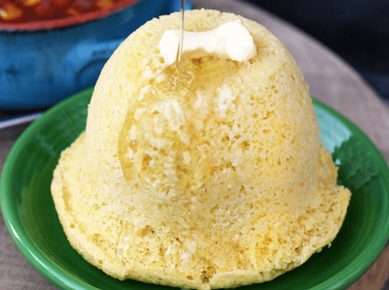 A green plate with cornbread made in a mug topped with butter and honey.