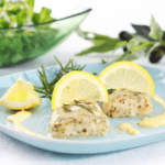 Two fillets of pan-roasted hake with greens in the background.