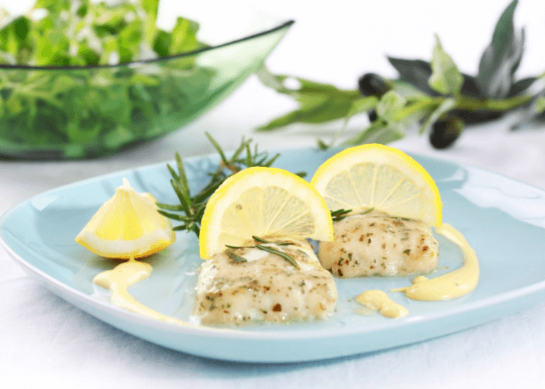 Two fillets of pan-roasted hake with greens in the background.