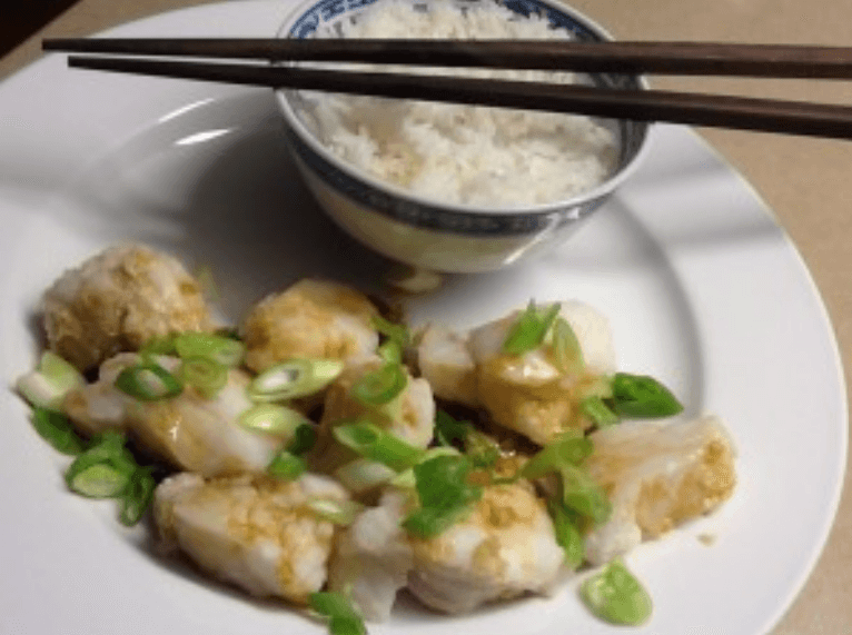 Steamed monkfish with ginger and spring onions served with a bowl of white rice.