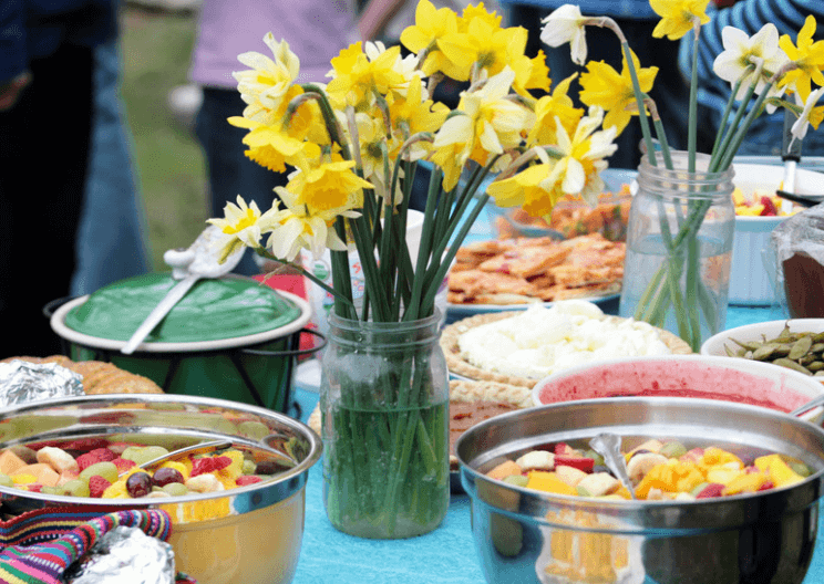 A table full of bowls of fruit salad and jars of yellow daffodils.