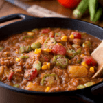 A black skillet with okra stew with a wooden spoon.