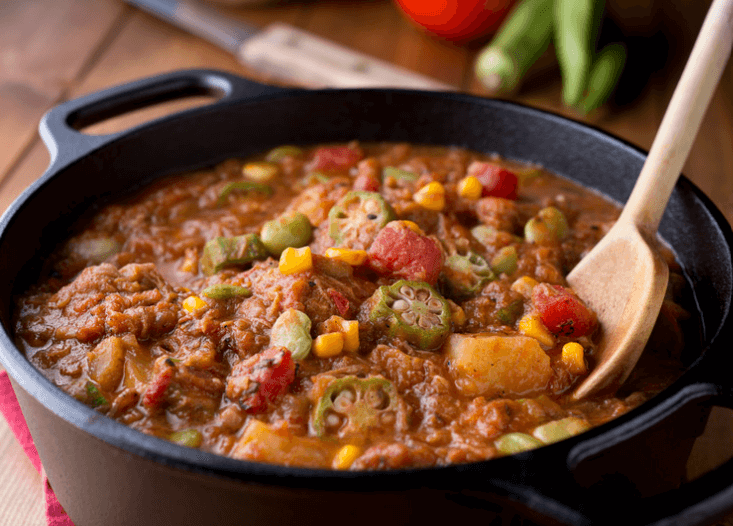 A black skillet with okra stew with a wooden spoon.