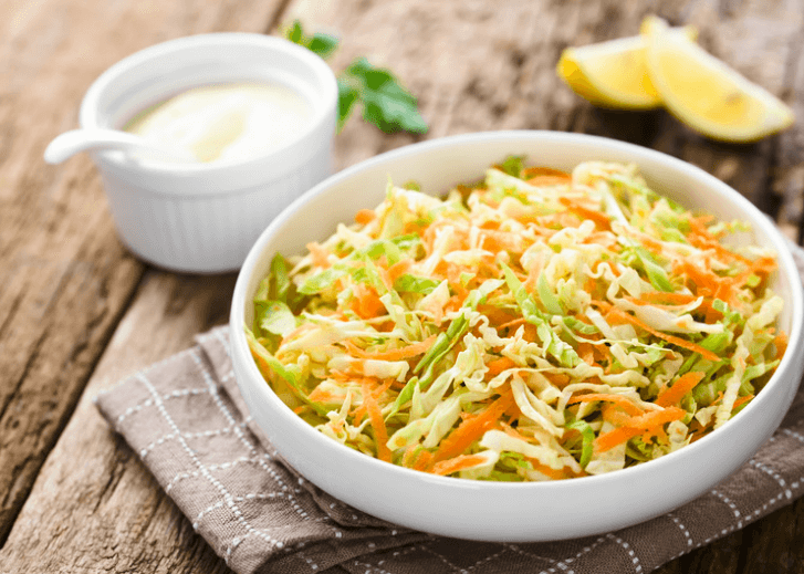 A large white bowl filled with carrot and kohlrabi slaw with a white sauce and lemon wedges in the background.