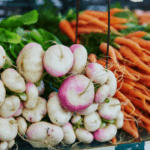 A large pile of turnips with another large pile of carrots in the background.