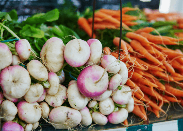 A large pile of turnips with another large pile of carrots in the background.