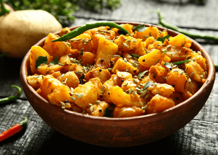 A large bowl filled to the top with a bright eggplant and potato curry.