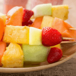 Several cut strawberry, pineapple, melon,, kabobs on a plate.