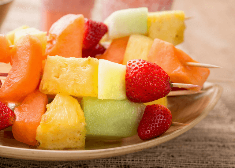 Several cut strawberry, pineapple, melon,, kabobs on a plate.