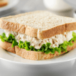 Tuna salad sandwich with lettuce on a white plate.