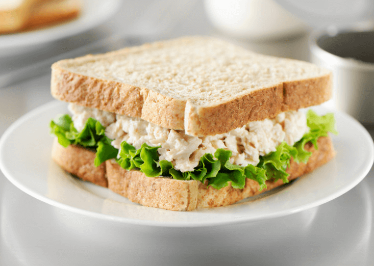 Tuna salad sandwich with lettuce on a white plate.